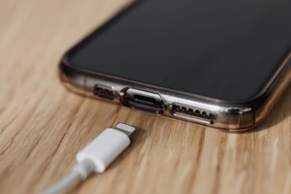 A charging cable next to the port of a smartphone on a wooden table