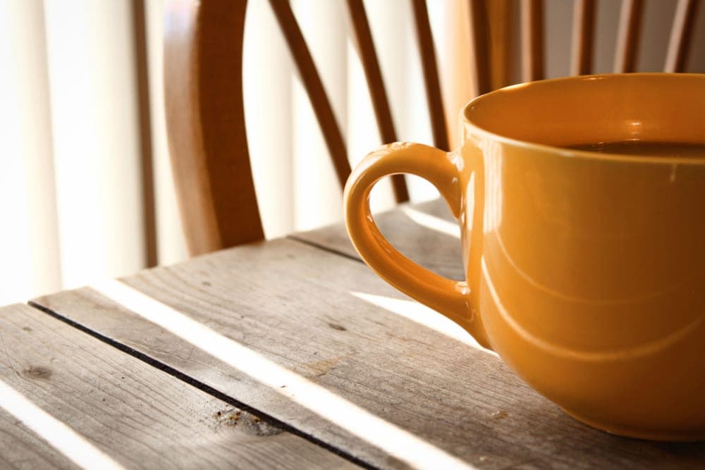 A yellow coffee mug on a wooden table in morning sunlight