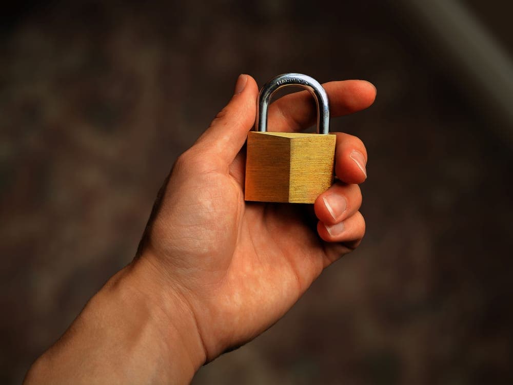 A hand holding a small brass padlock against a dark background