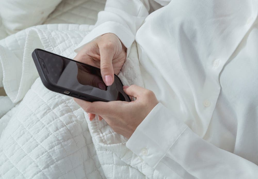 Hands holding a smartphone over a white quilted bedspread