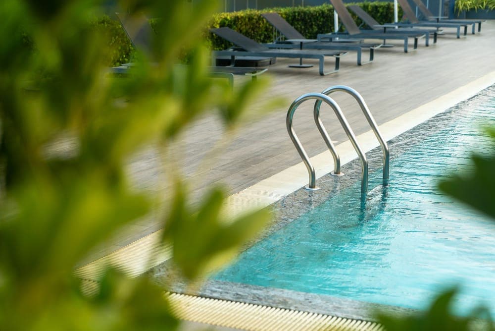An outdoor swimming pool with a steel ladder, seen through green leaves