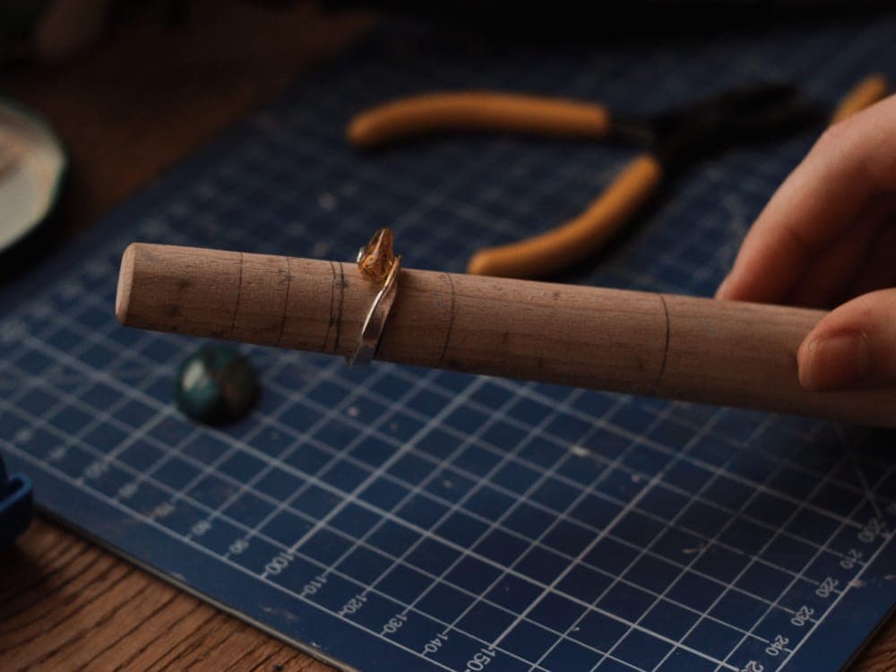 A wooden ring mandrel with size marks and a silver ring on it