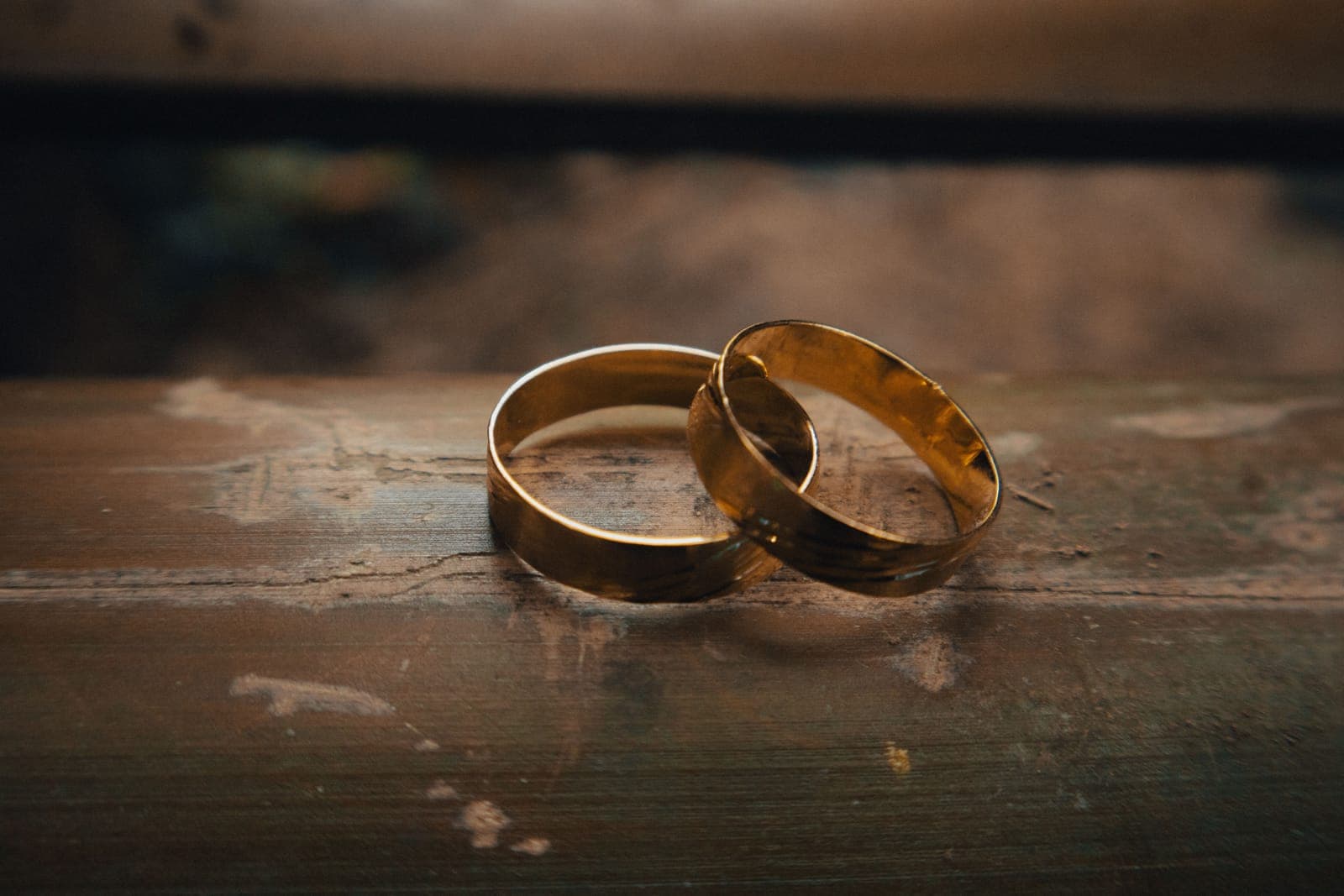 Two plain gold bands resting together on a weathered wooden surface